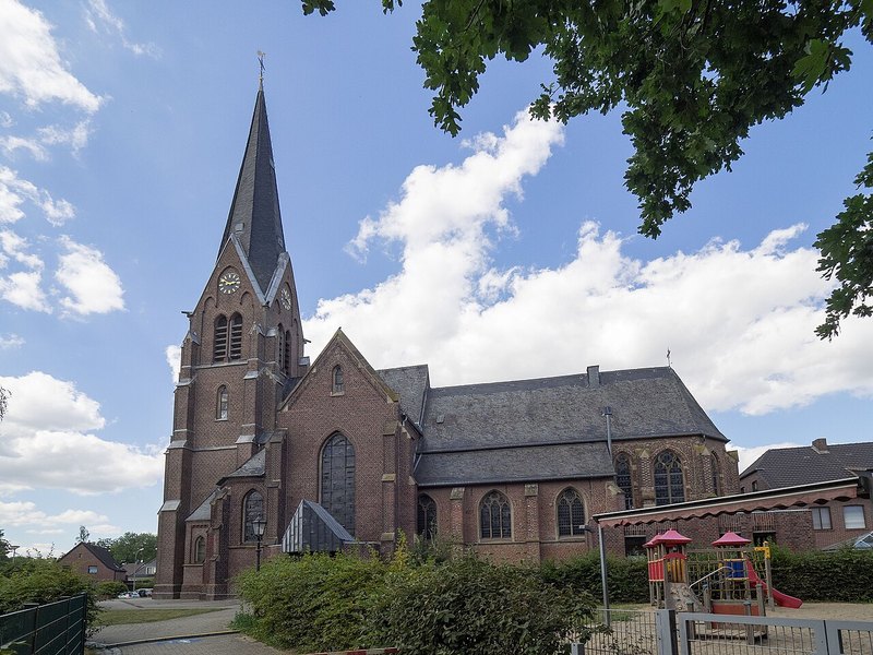 St. Peter in Boisheim mit Kirchturm links und langem Kirchenschiff rechts unter blauem Himmel