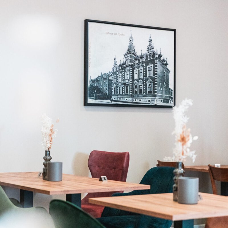Holztische und gepolsterte Stühle im Café Tante Anna; an der Wand hängt eine historische Stadtansicht.