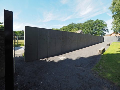 Lange dunkle Gedenkmauer in der Gedenkstätte Waldniel-Hostert neben einem Kiesweg.