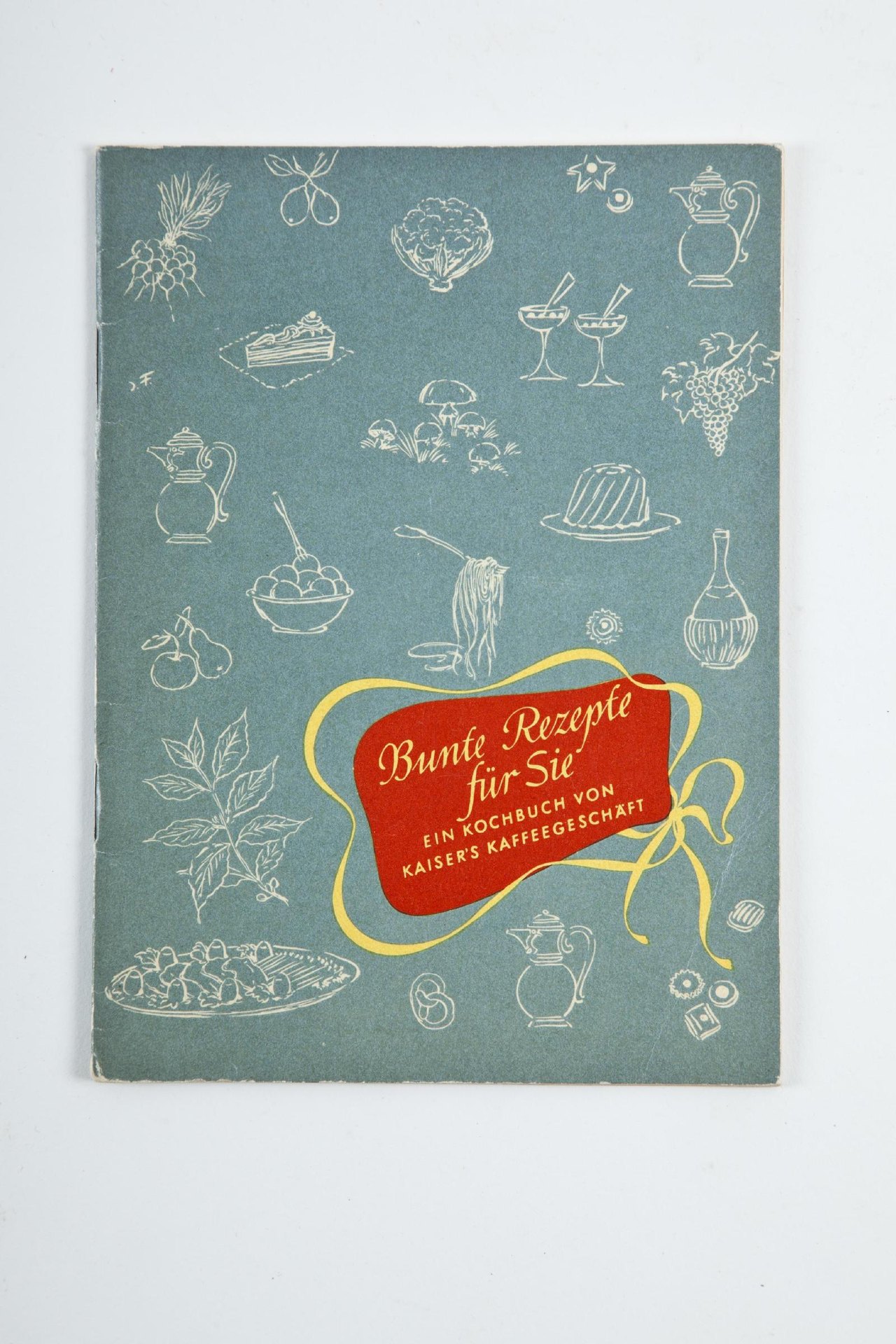 Umschlag von Bunte Rezepte für Sie: hell gezeichnete Lebensmittel und Kaffeekannen auf graugrünem Grund, dazu ein rotes Titelfeld mit gelber Schrift.